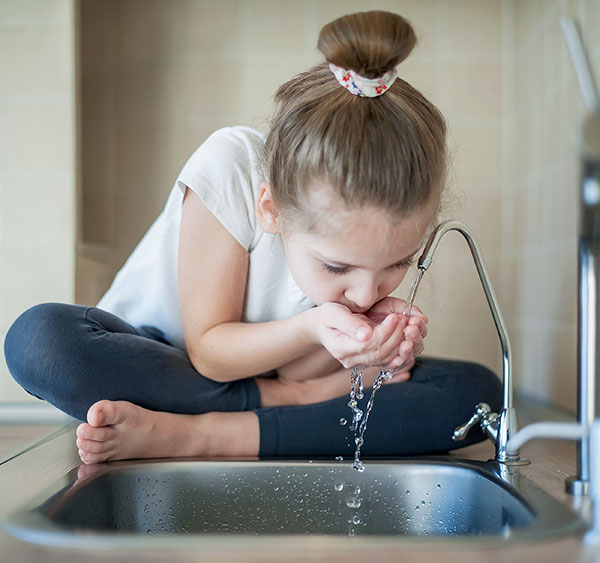 Kind trinkt Wasser am Hahn